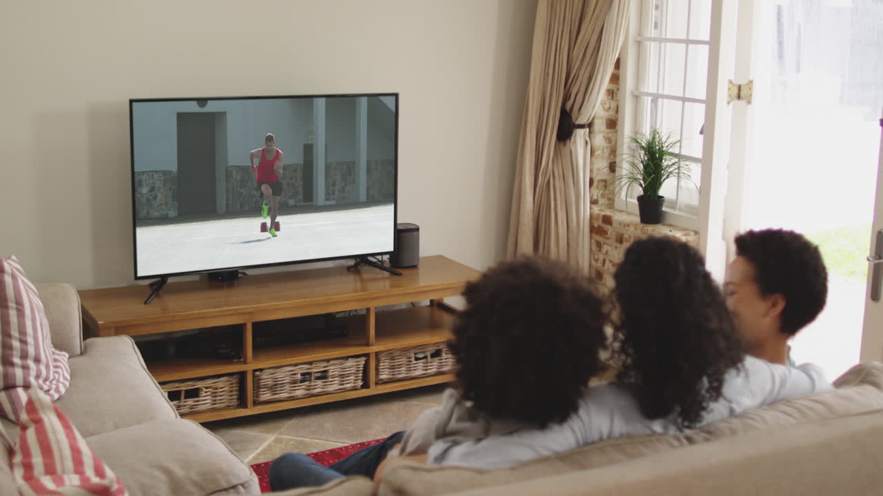 Famiglia felice seduta a casa insieme che guarda la corsa di atletica in TV