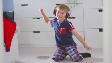 Niño-En-Casa-En-El-Dormitorio-Usando-Auriculares-Inalámbricos-Escuchando-Música-En-Una-Tableta-Digital