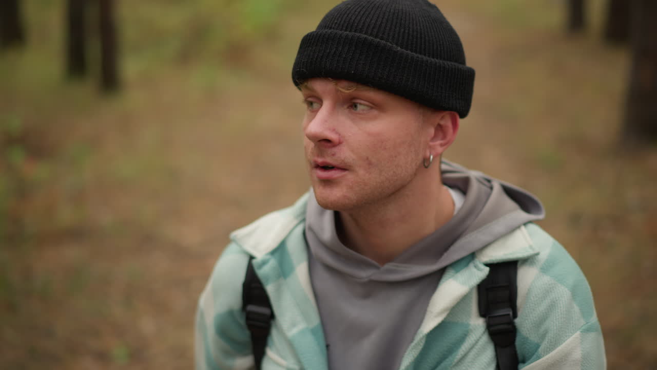 Jeune voyageur blanc enlève son bonnet et se tient le front. Un portrait rapproché capture son soupir et son expression de fatigue après une randonnée. Un moment spontané de fatigue, de réflexion et de récupération tranquille en tant que randonneur et voyageur.