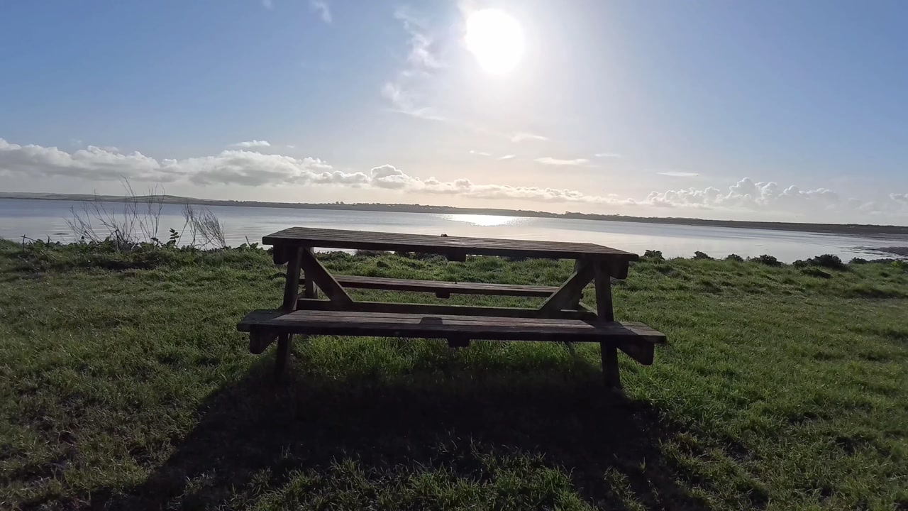 Empty wooden park picnic table looking out across ocean beach coast in morning sunlight