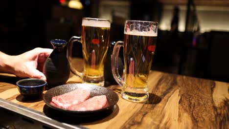 person seasons steak beside two beer mugs