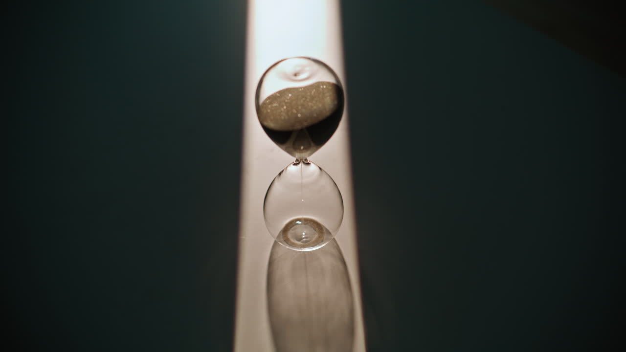 Man hand turning hourglass on table with evening shadow closeup. Time countdown