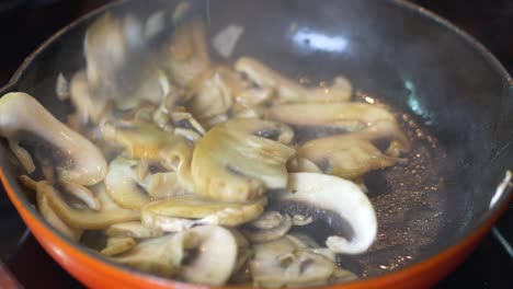 sliced mushrooms are frying in a hot red pan