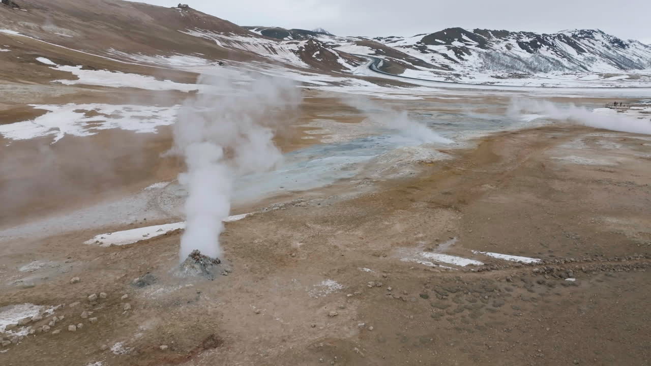 vista aérea de la zona geotérmica activa en el paisaje de islandia, vapores, ollas de barro y colinas nevadas