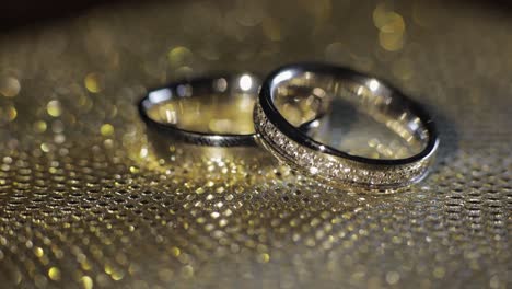 wedding rings lying, rotate, spinning on shiny golden shining surface with light, close-up macro