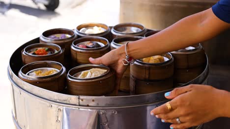 hands arranging bamboo baskets of dim sum on a steaming tray, under natural lighting, showcasing a culinary preparation process