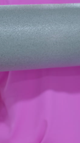 primer plano de una mano de mujer sosteniendo una espuma de rodillo, con un anillo en su dedo, mientras empuja hacia adelante, con una vista parcial de otra persona en el fondo en un entorno de gimnasio
