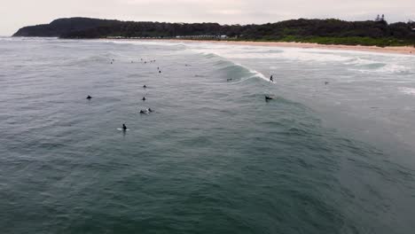 Toma-Panorámica-De-Drones-De-Un-Gran-Grupo-De-Surfistas-En-La-Playa-Lluviosa-De-Shelly-La-Entrada-De-La-Costa-Central-Nsw-Australia-4k