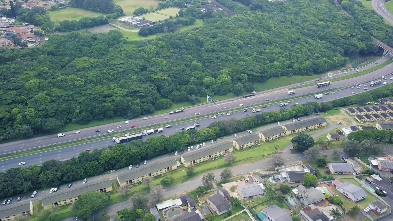 주거 주택 위를 날아다니는 드론의 공중 영상, 노란 나무 공원 더반의 교외에서 이동하는 교통과 함께 바쁜 고속도로를 내려다보고 있습니다.