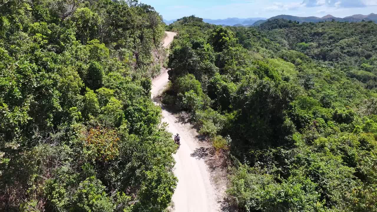 Drone follow man on dirt road riding motorbike on Busuanga Island coast, Philippines.