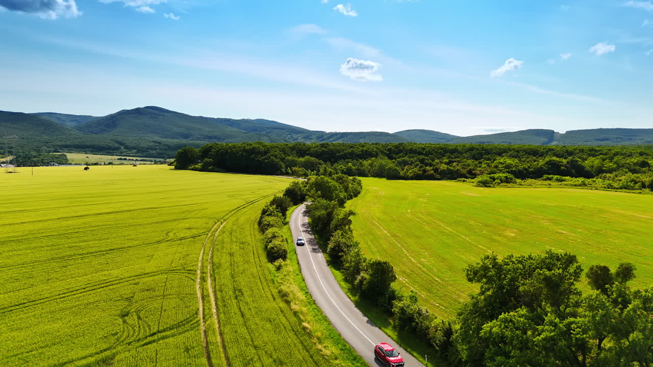 Scenic road through green fields. A winding road curves through lush green fields under a bright blue sky, surrounded by distant hills and trees