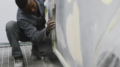 African-American-male-car-mechanic-working-in-a-township-workshop-and-polishing-a-side-of-a-car