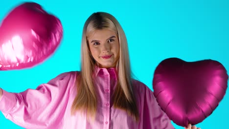 Mujer-Bonita-Rubia-Sosteniendo-Globos-De-Corazón-Púrpura-Agitando-Mientras-Mira-La-Cámara,-Foto-De-Estudio-Colorida