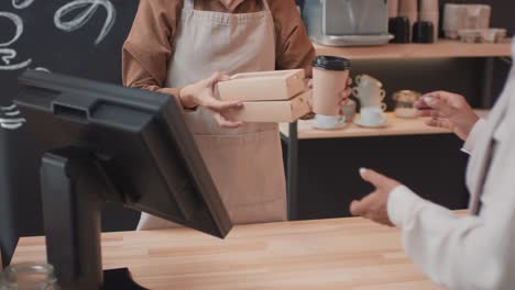 waitress in apron sells a customer a takeaway coffee and food behind the counter in a coffee shop