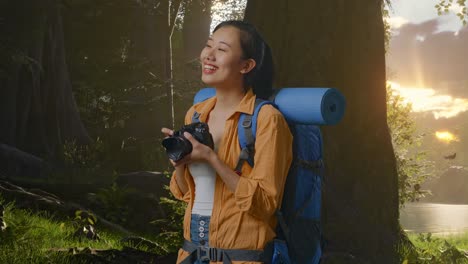 side view of asian female hiker with mountaineering backpack smiling and holding a camera in her hands then looking around while exploring forest nature