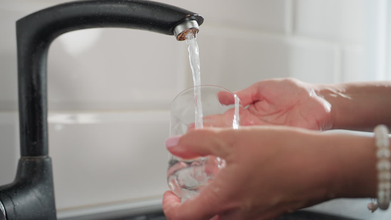 Close up of glass cup being thoroughly rinsed under neat running water at kitchen sink with clear flowing stream highlighting focus on cleanliness hygiene sparkling transparency