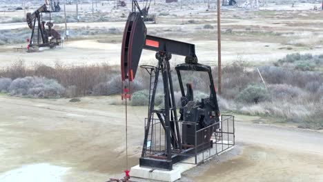 Oil-well-drilling-derricks-or-pumpjacks-for-crude-oil-production-in-a-desert-landscape,-aerial-view