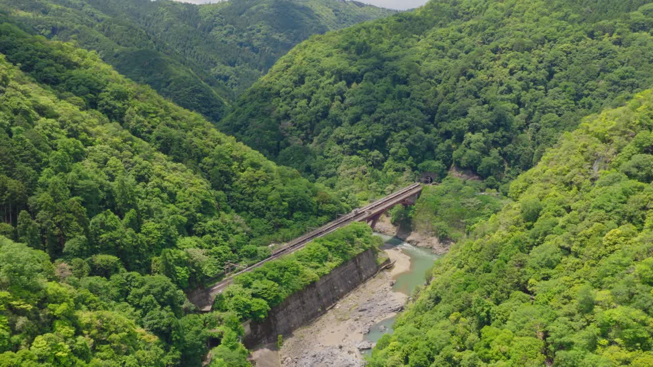Aerial fly bridge cross above Arashiyama River in Kyoto Japan forested Mountains, lush green landscape