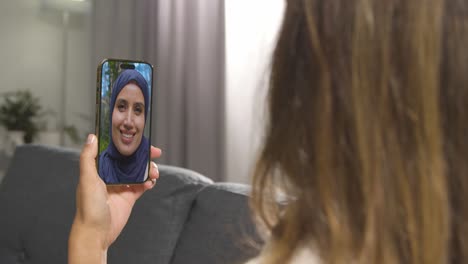 primer plano de una mujer sentada en el sofá en casa haciendo una llamada de video con una amiga musulmana en el teléfono móvil