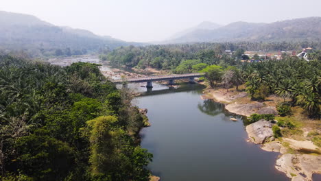 aerial reveal of scenic road bridge spanning rocky river in india