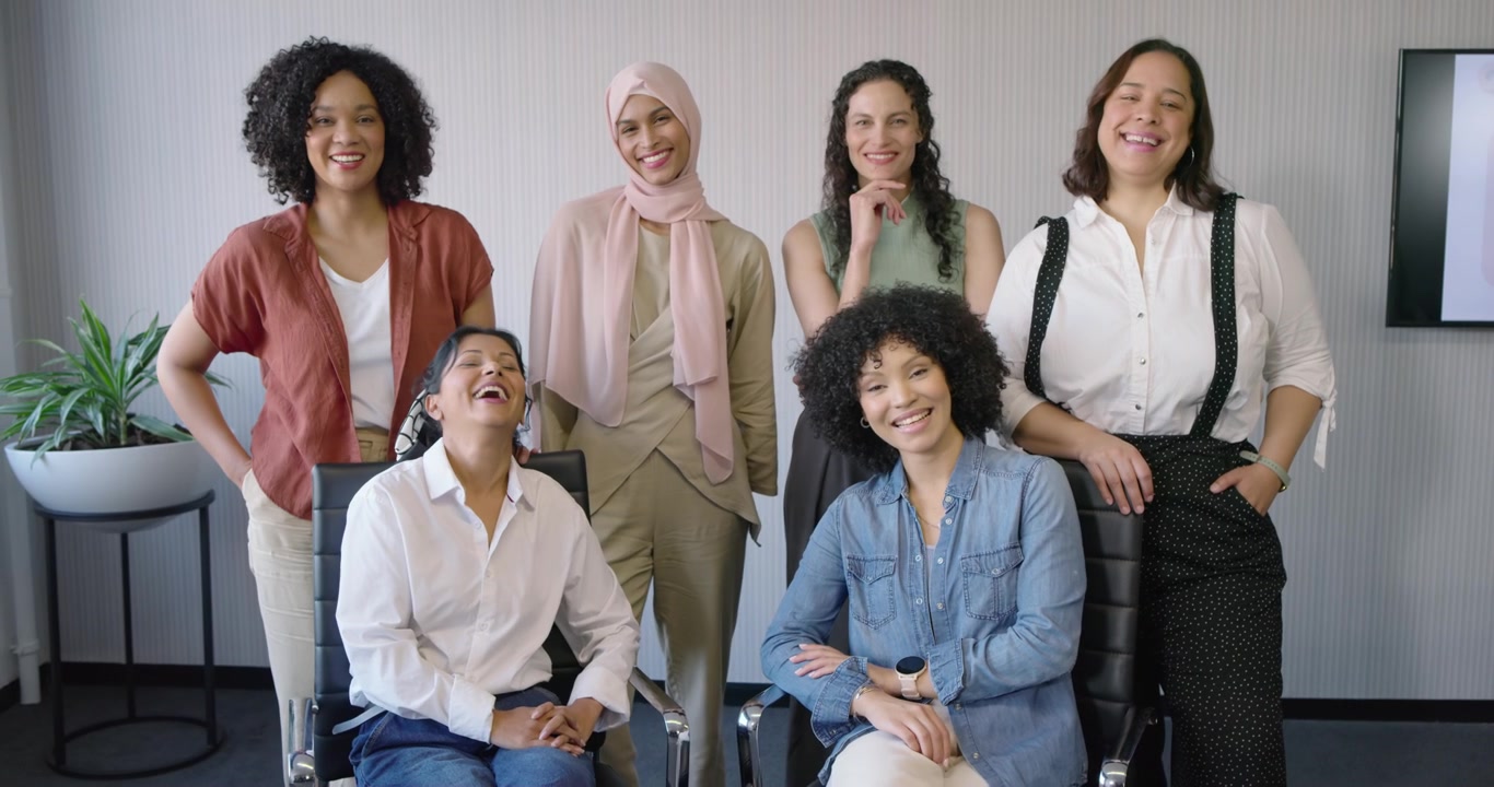 Diverse female team relaxing into smiles while posing for portrait in conference room with chairs