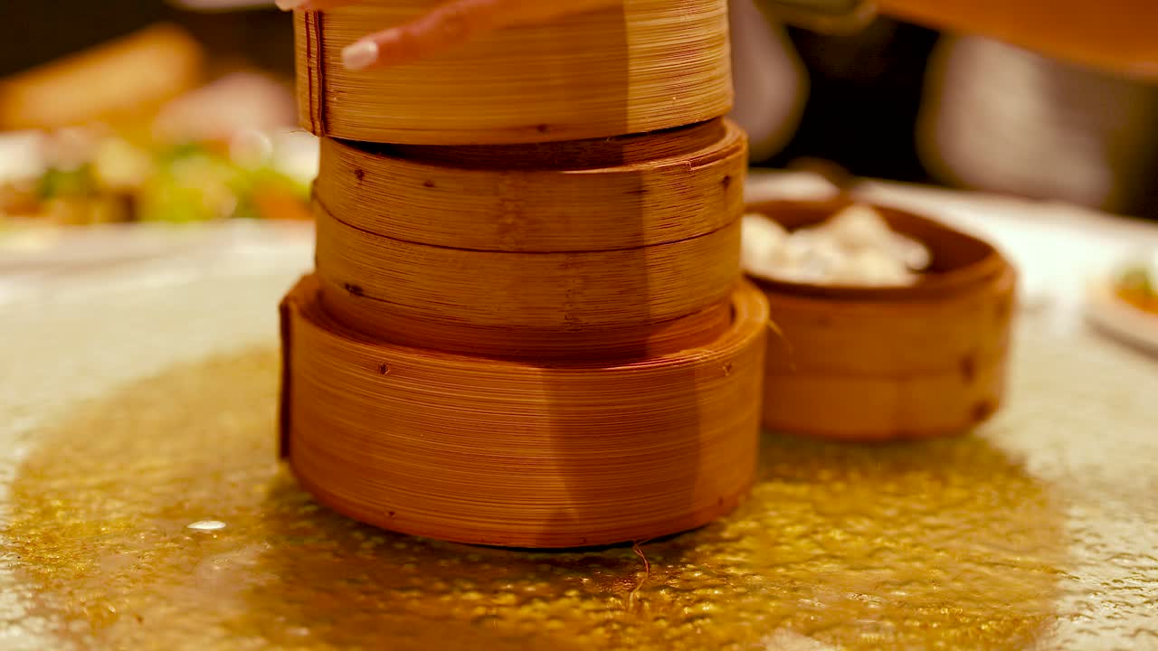 Hands serve dim sum from bamboo steamers in a warm, inviting restaurant setting with ambient lighting