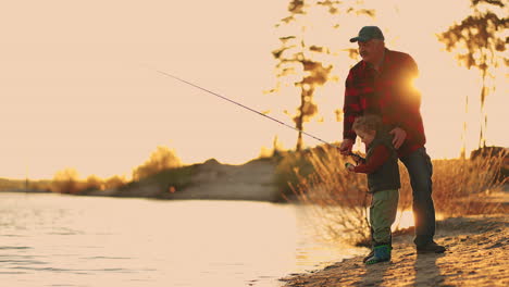 Fin-De-Semana-Activo-En-La-Naturaleza-El-Anciano-Y-El-Niño-Están-Pescando-En-La-Orilla-Del-Río-Al-Atardecer