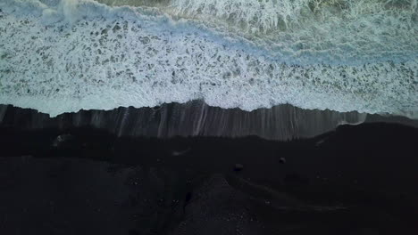 top down drone aerial of waves coming up onto the black sand beach near vik in iceland