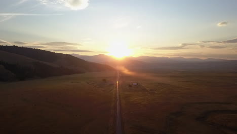 aerial rises over pasture land as golden sun sets on rocky mountains