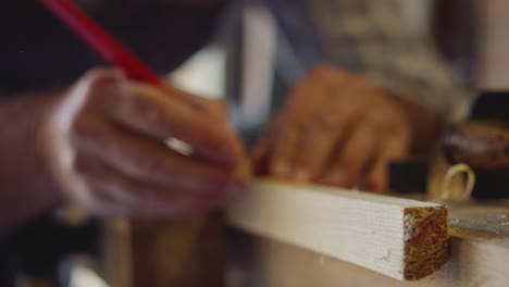 close up of male carpenter in garage workshop measuring and planing piece of wood