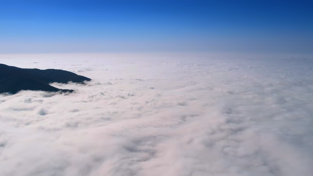 Dark mountain silhouettes peeping out of thick white cloudscape hiding the land. Aerial view