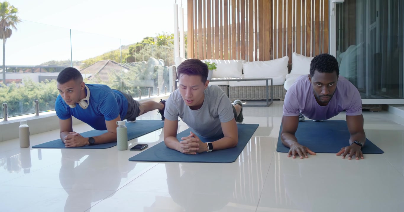Diverse male friends exchanging taps, shifting into forearm planks on blue mats for core on balcony