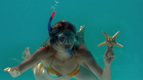 mujer con snorkel sosteniendo estrellas de mar bajo el agua