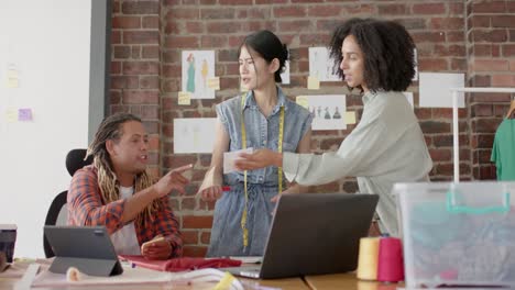 diversos diseñadores ocupados usando portátiles y discutiendo el trabajo en el estudio de diseño de moda en cámara lenta