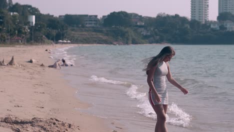 girl with long hair walks on wet beach sand by ocean waves