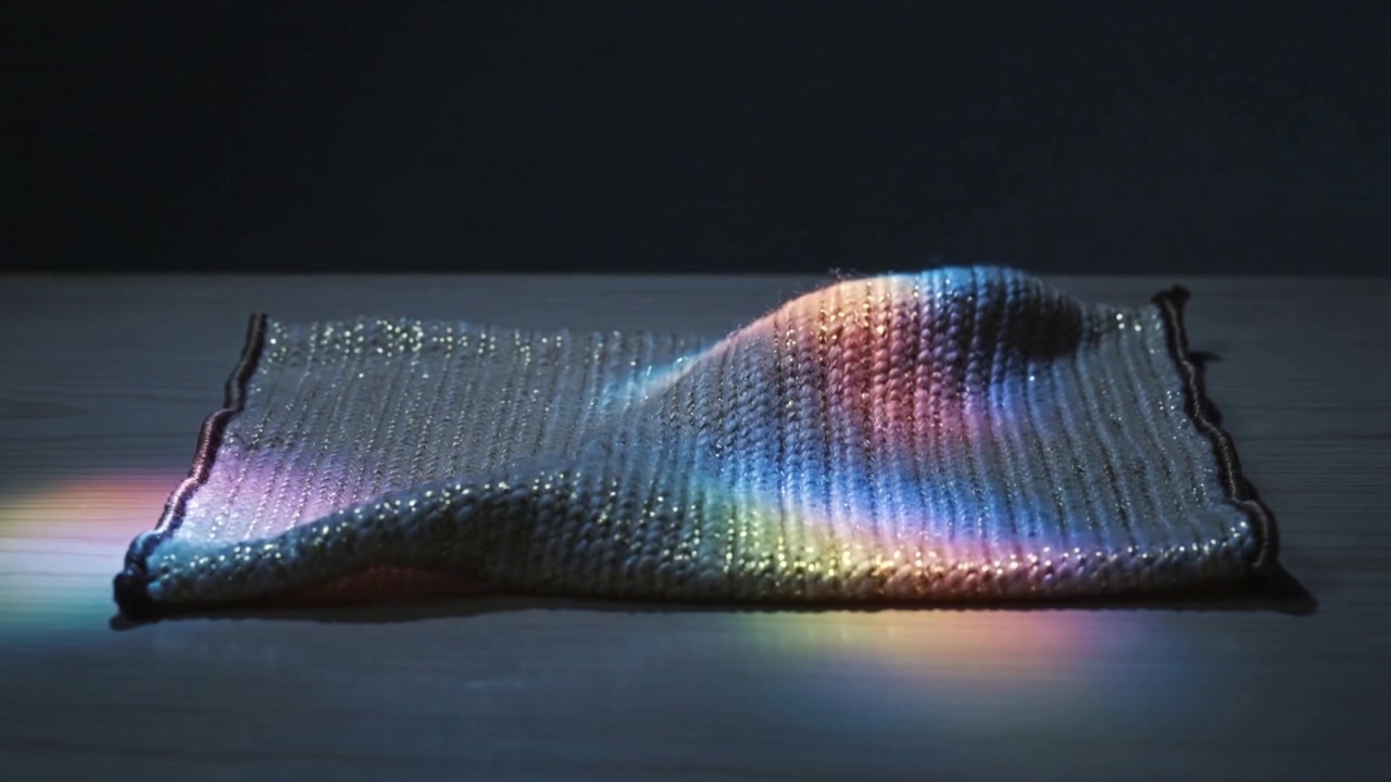 Projecting light hitting sequined mat, forming rising mound on tabletop while rainbow bands sliding
