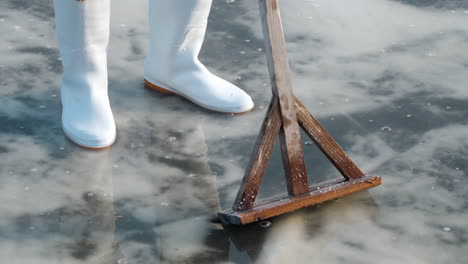 person in white boots standing at a salt flat with a wooden rake at gaetgol eco park in south korea