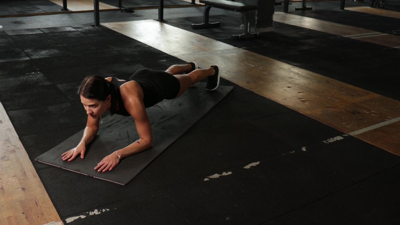 Donna determinata che mantiene la posizione del plank sul tappetino in palestra