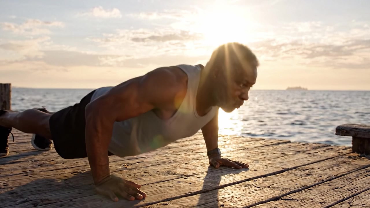 Un anziano ispiratore che esegue flessioni su un molo sereno al tramonto, mostrando forza, determinazione e impegno per la forma fisica nella bellezza della natura