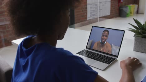 African-american-woman-talking-on-video-call-with-male-colleague-on-laptop-at-office