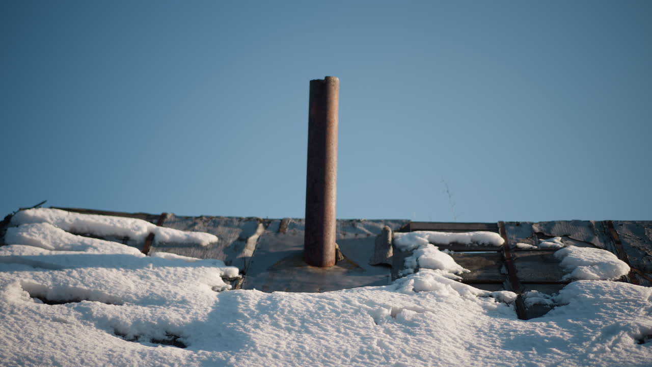 Snedækket hustag med udluftningsrør. Bredt udsyn over snedækkede tagsten og rustent lodret rør mod klar blå himmel, skarpt morgenlys, teksturerede granuler, diskret forfald på metal, ideelt.