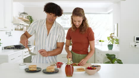preparing breakfast, diverse couple slicing strawberries and stacking pancakes in kitchen, at home