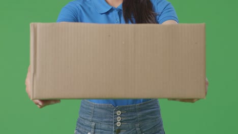 close up of a female courier in blue uniform showing a carton to camera while delivering it on green screen background in the studio