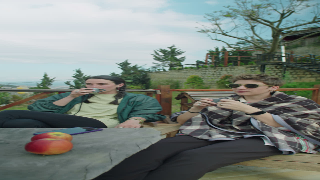 Young Women Enjoying View and Talking over Tea at Glampsite