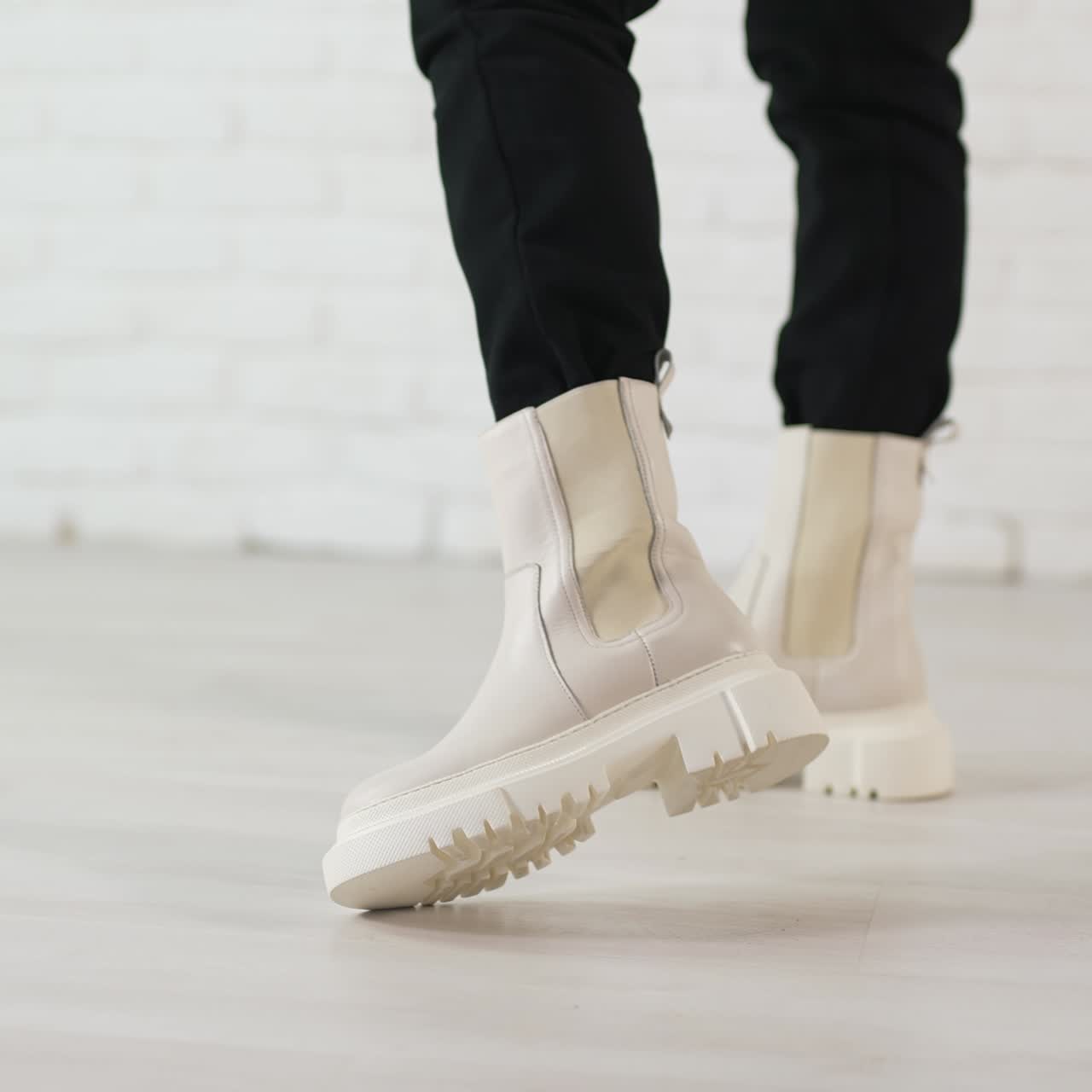 Woman in black jeans walks in new stylish white boots. Demonstrating the shoes of top fashion. White brick wall backdrop