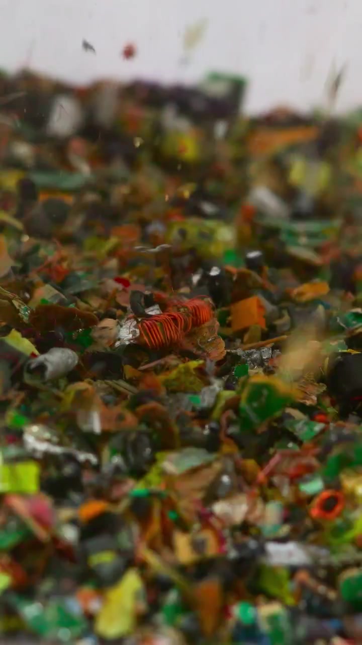 Primo piano di frammenti di plastica colorati macinati all'interno di un frantoio industriale e un nastro trasportatore, polimeri misti e minuscoli.