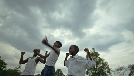 Niños-Africanos-En-Uniforme-Comparando-Músculos-En-El-Cielo-Nublado-En-Uganda