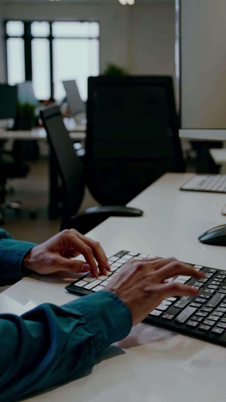 A close-up, side-angle shot of hands typing on a keyboard in a modern office