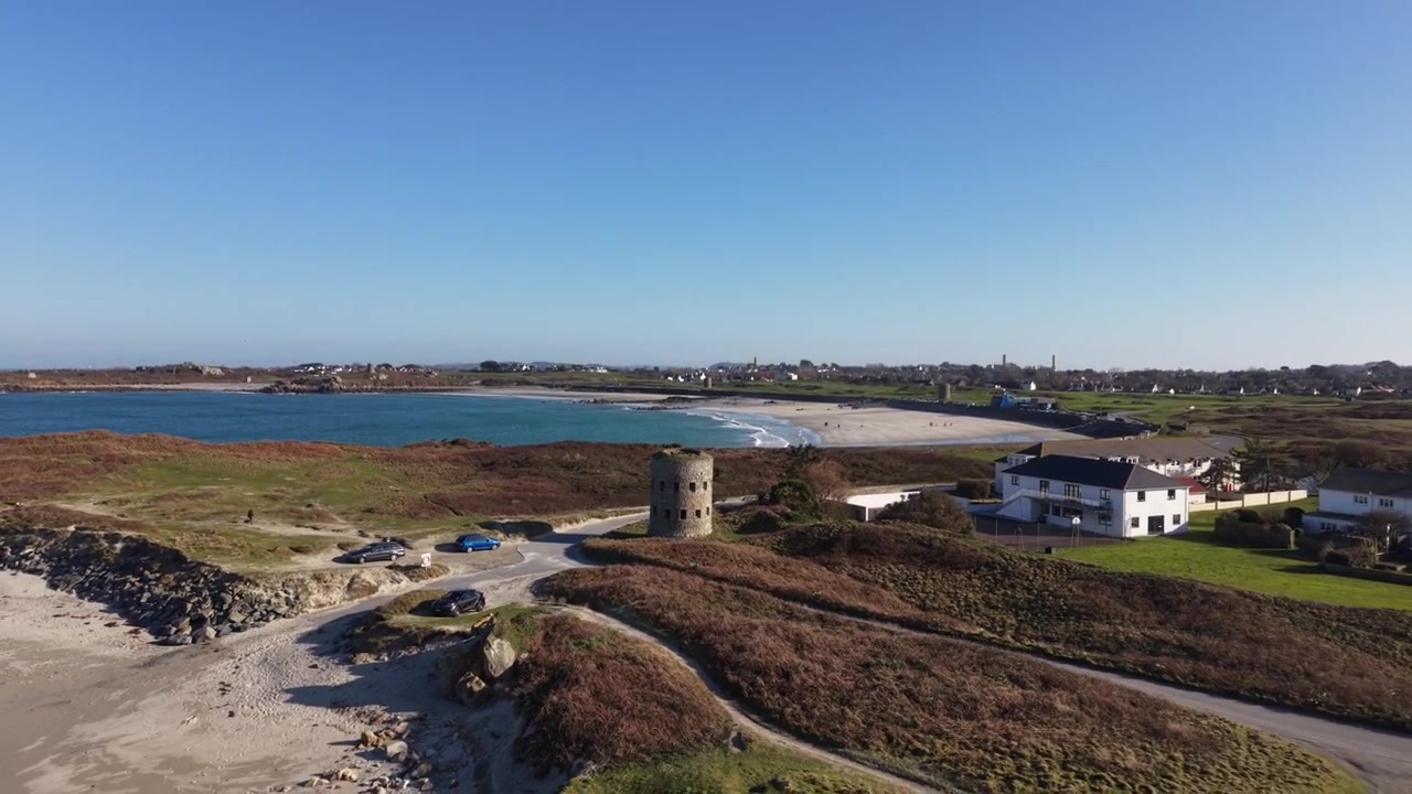 Torre Martello, Pembroke Vale, Guernsey. Rapida rivelazione della torre, The Bay Apartments e Lancresse Bay e Common, ottima prospettiva di una bellissima spiaggia sotto il sole del tardo pomeriggio con cielo azzurro limpido.