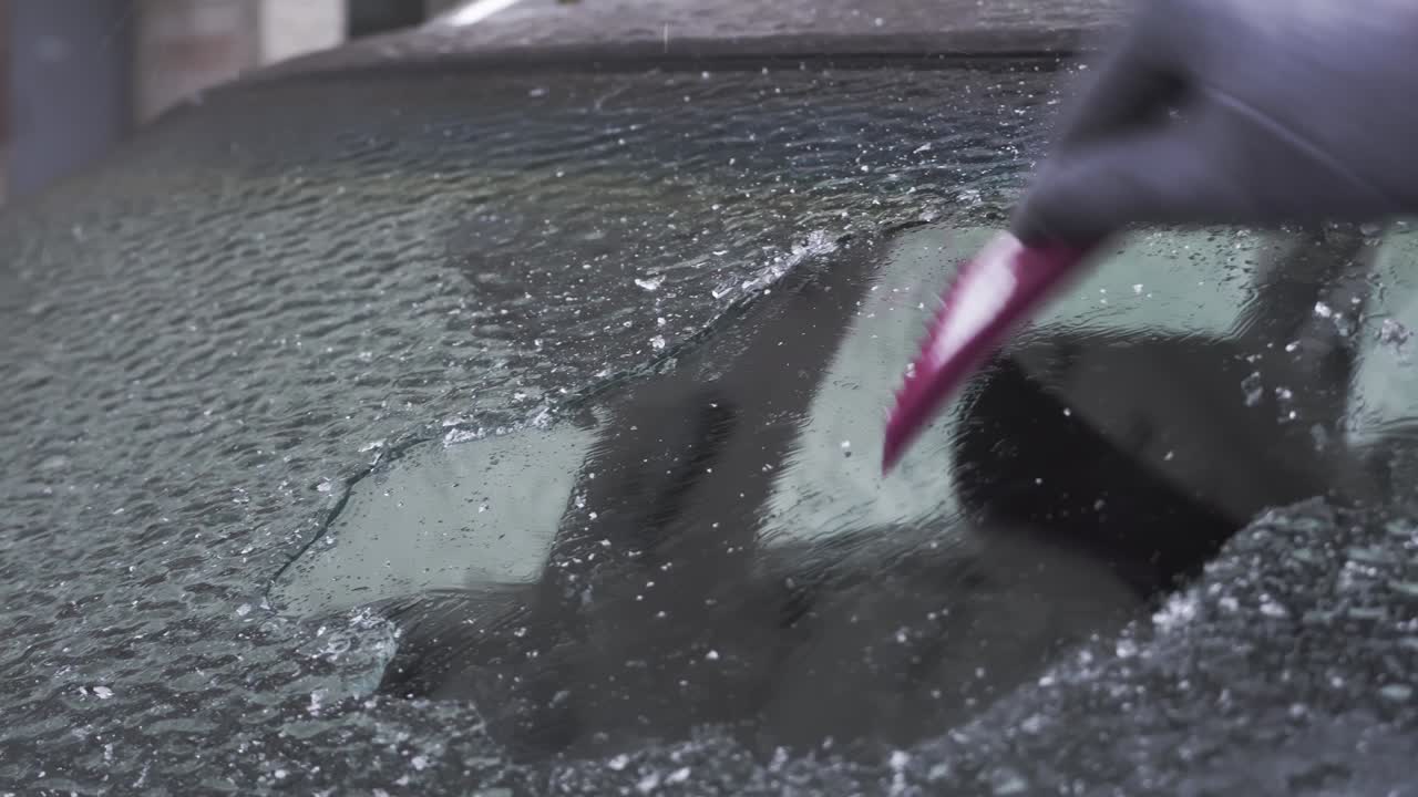 una mujer raspa el hielo del parabrisas de su coche después de un largo estacionamiento.